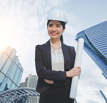 Business woman in a hard hat in front of sky scrapers.